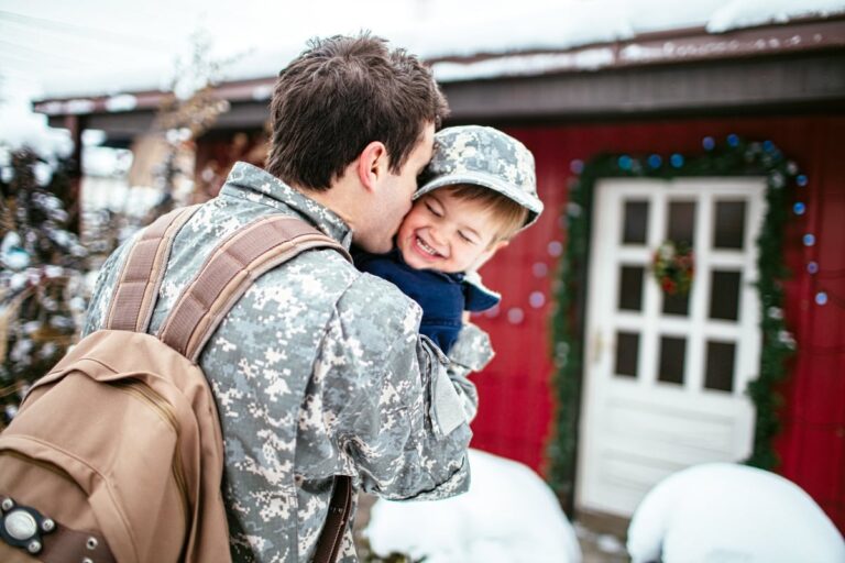Military father with backpack hugging child outside home 8VBdkeF