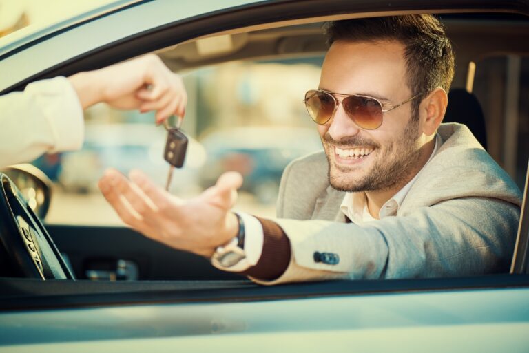 a smiling person sitting in their car holding their hand out the window to take keys off another person