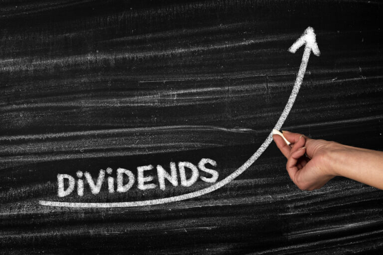the word dividends on a chalkboard with a person drawing an upward arrow