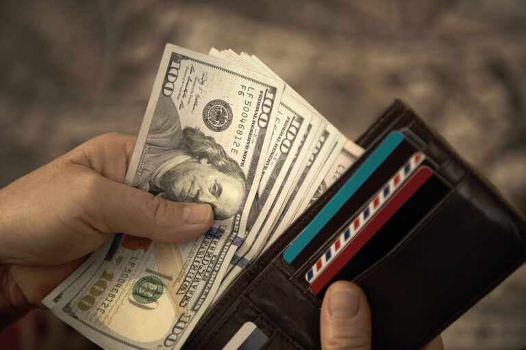 person placing hundred dollar bills into a wallet