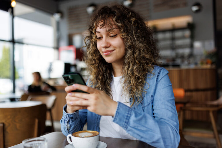 smiling person looking at smartphone in coffee shop