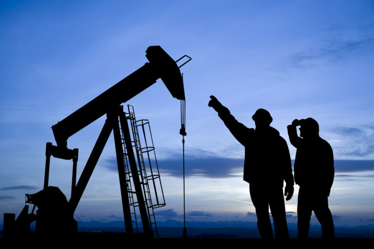 the silhouette of some people pointing to an oil well