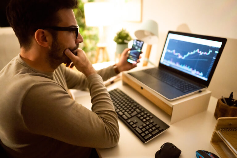 person looks at stock charts on their computer and phone getty