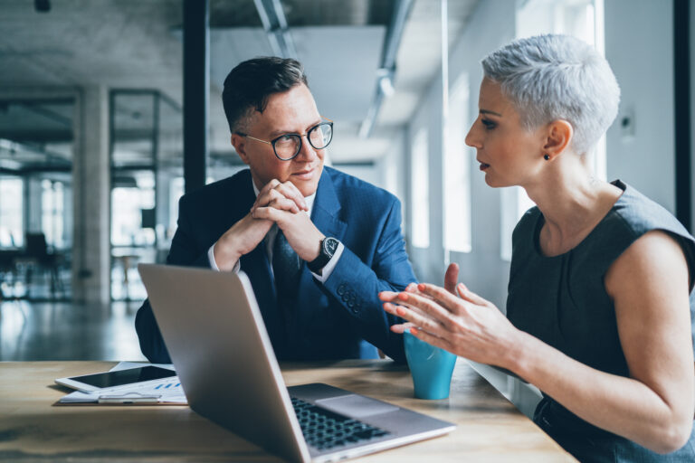 two businesspeople talking in front of a laptop