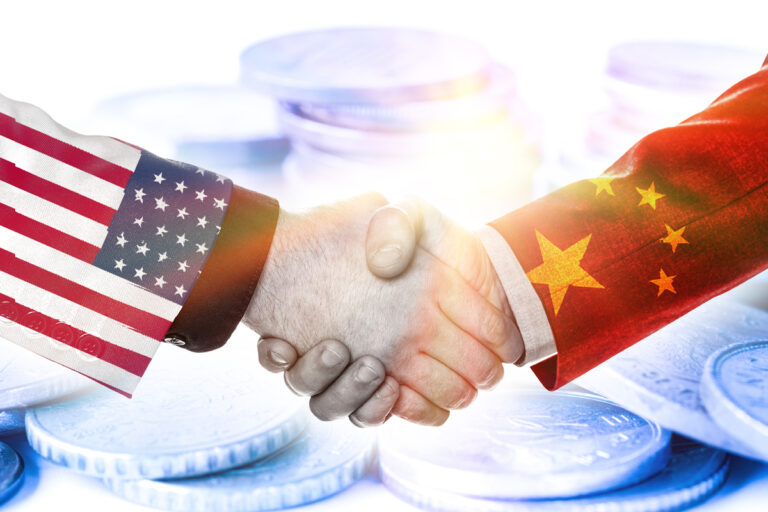 a handshake featuring one arm dressed with an american flag and another with a chinese flag with coins in the background