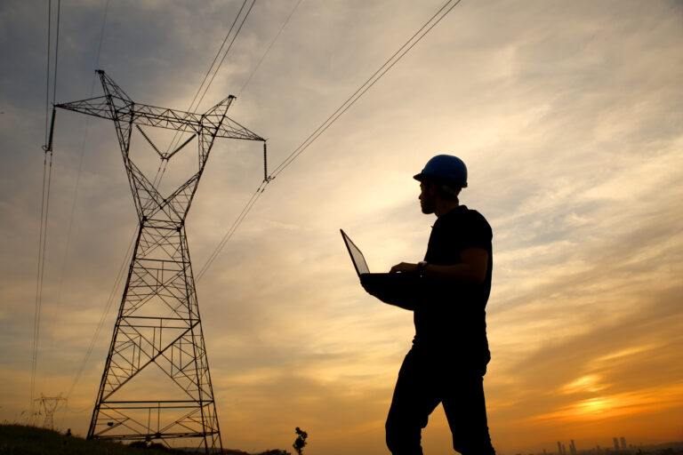 a person wearing a hardhat and holding a laptop near a power line