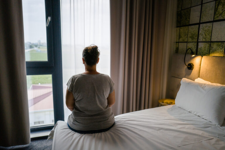 person on a hotel room bed gazing out the window
